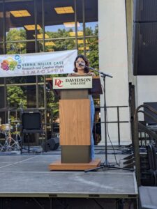 Photo of Mishti Mookherjee standing behind a Davidson College podium, speaking to the public. 