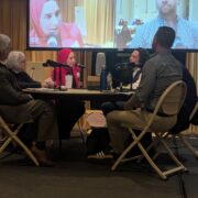 photo of panelists sitting around a table with a screen in the background.