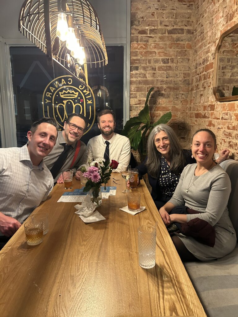 Panelists sitting together at a bar smiling at the camera