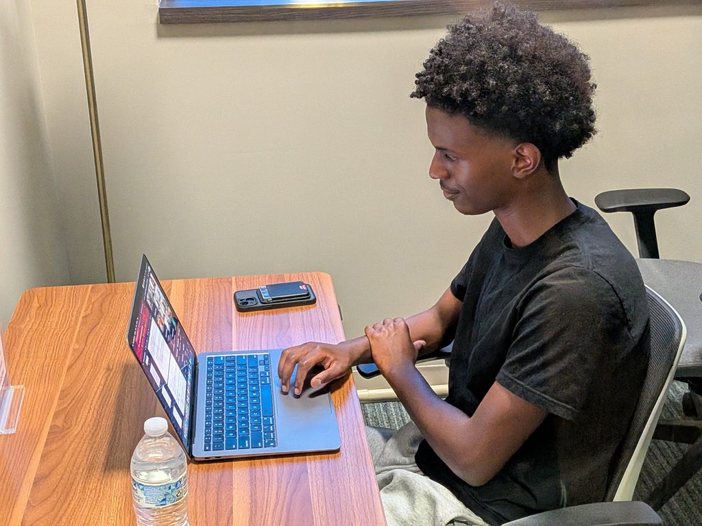 A student seated at a wooden desk participating in a virtual session or online deliberation on his laptop.