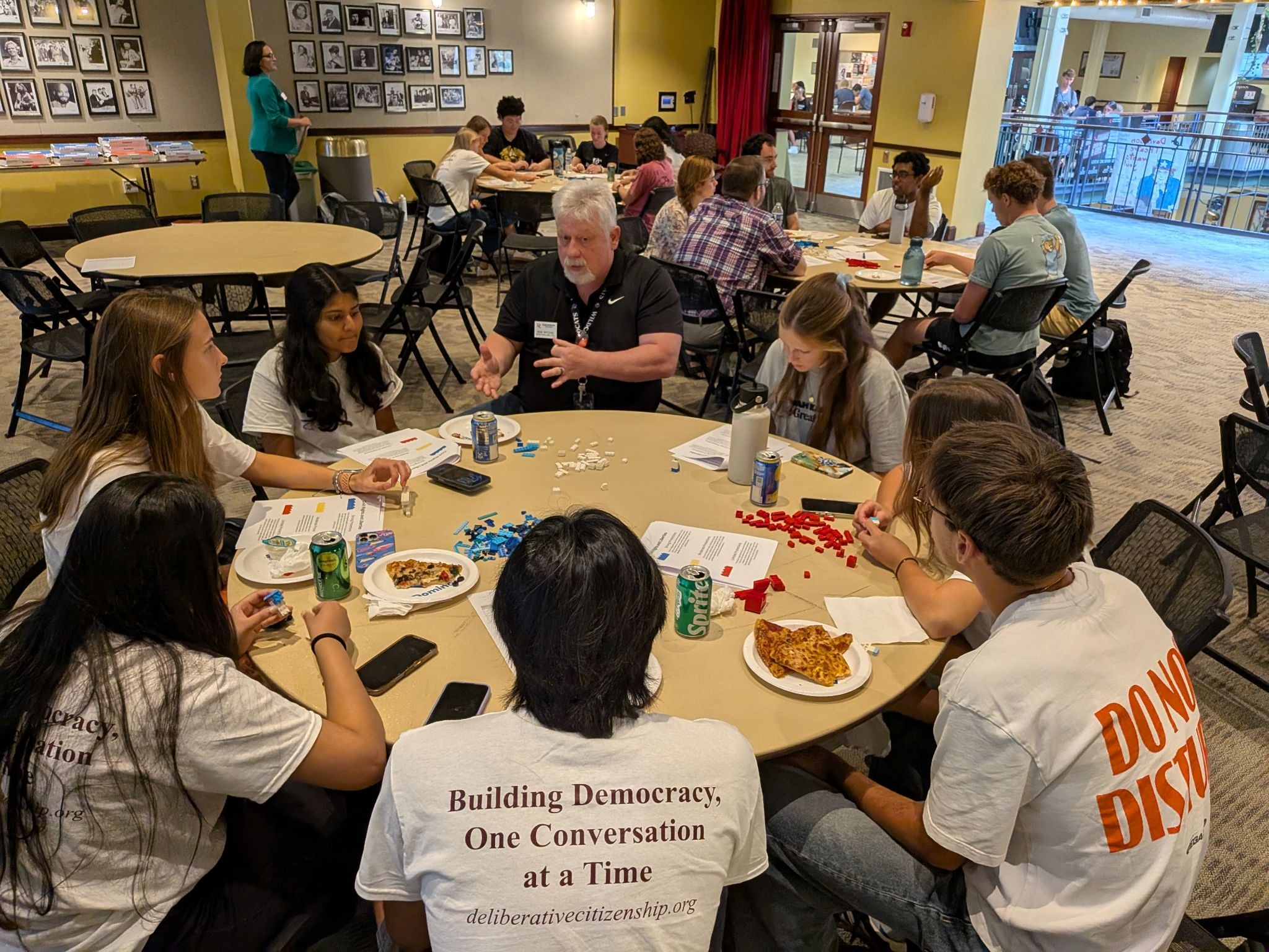A photo of a workshop or group discussion where participants sit at round tables with red, blue and white Lego bricks.